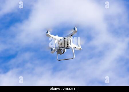 Quadcopter drone is flying in the blue sky. Unmanned aerial vehicle. Remote video shooting from a height. Modern digital camera. Stock Photo