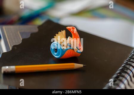 Pencil sharpener with pencil. Sharpened wooden pencil on a black notebook. The concept of training, education. Side view. Selective focus. Close-up. Stock Photo