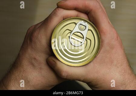 Two Hands of an Adult Man holds a can of canned food. Closed tin can with open key in hand. Canned foods. This really canned product. Selective focus. Stock Photo