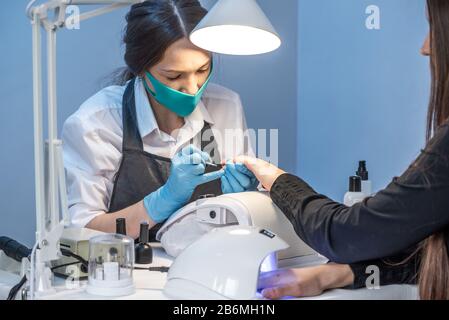 A woman manicure master in the salon in the process of working with the client 's nails on a blue background. Cosmetology and nail care Stock Photo