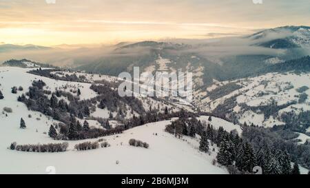 Beautiful bewitching view of mountains and rocks with spruce forest on a frosty winter evening with fog and sunset sun. Harsh winter nature concept Stock Photo