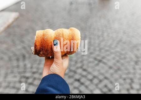 Woman holds in hand Trdlo or Trdelnik, it is a national street food on the background of city tourist streets of Prague Stock Photo