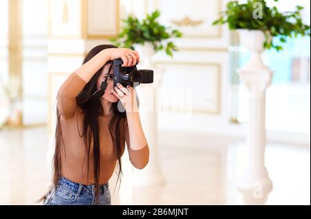 Modern female photographer with photo camera taking pictures of interior while standing in light vintage room Stock Photo