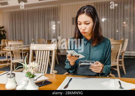 dissatisfied customer woman in the restaurant after dinner gets money out of her wallet to pay the bill, the concept of expensive prices in a cafe Stock Photo