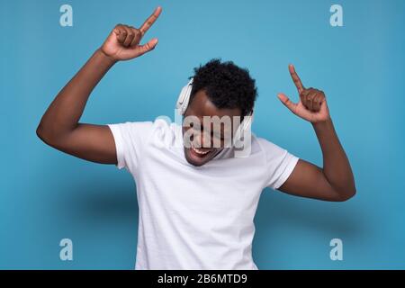 African American man with whie headphones dancing on blue background Stock Photo