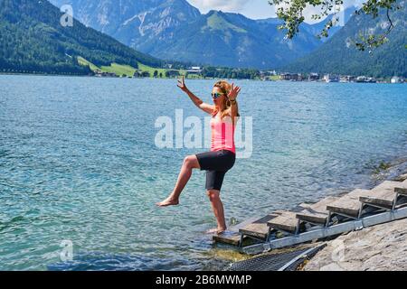 Lady tourist balancing on one foot at the edge of Achen Lake (Achensee), Tirol, Austria, on a bright sunny Summer day. Stock Photo