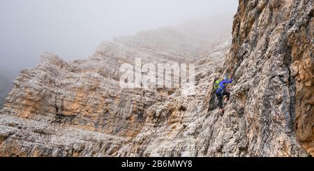 Woman on via ferrata Cesare Piazzetta, moving up through the low clouds. Active holiday in Sella group, Dolomites mountains, Italy. Stock Photo