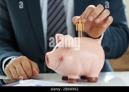 Male manager putting small wooden human figure into piggybank Stock Photo