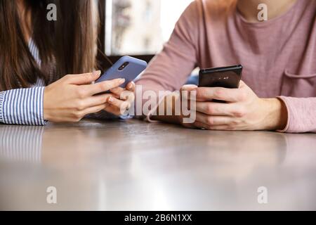 Close up of a young couple using mobile phones while sitting at the cafe table indoors Stock Photo