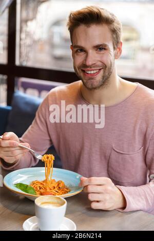 Smiling young man having lunch while sitting in the cafe indoors, eating pasta Stock Photo