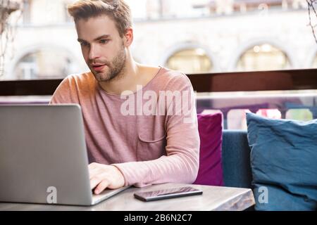 Handsome pensive young man working on laptop computer while sitting in the cafe