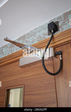An electronically controlled door closer mounted on a hardwood corridoor fire door in a block of luxury apartments. Chrome finish. Stock Photo