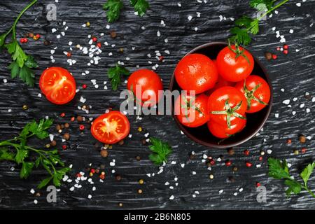 Fresh Sliced Cherry Tomatoes on a black background with spices coarse salt and herbs. Top view, use as cooking ingredients Stock Photo