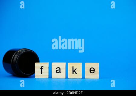 The word FAKE on wooden cubes and a medical dark flask on a blue background. Medical concept of counterfeit drugs Stock Photo