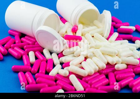 Two white pill jars and scattered pink and white capsules on blue background Stock Photo