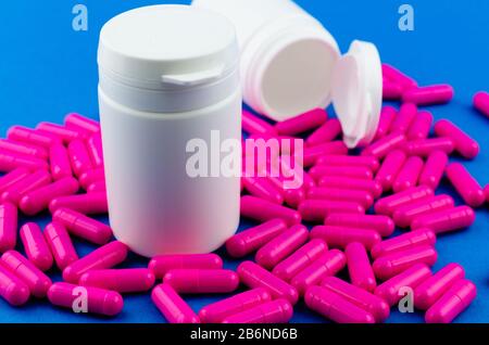 Two white pill jars and scattered pink capsules on blue background Stock Photo