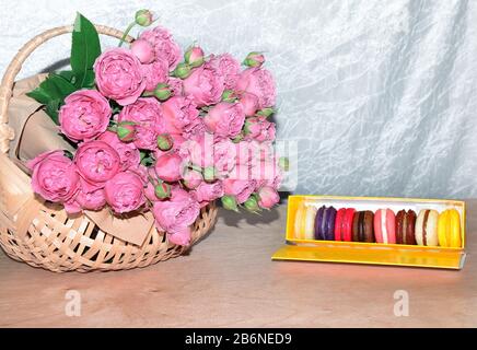 roses in a basket and macaroons, sweet and colorful French sweets, dessert on a light background, close-up Stock Photo