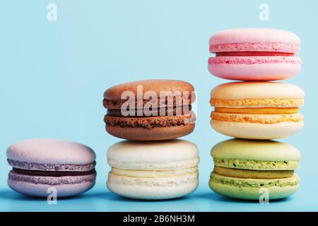 Multicolored French macaroni macaroni cookies are arranged in a pyramid on a blue background. Free space, close-up. Minimalistic concept Stock Photo
