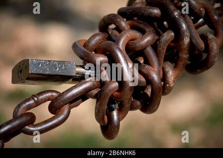 detail of a piece of twisted metal chain with a padlock in the field outdoors Stock Photo