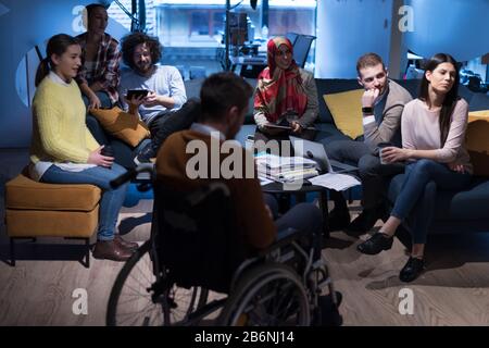 Handicapped young man with colleagues working in office. He is smiling and passionate about the workflow. Performing in co-working space. Office peopl Stock Photo