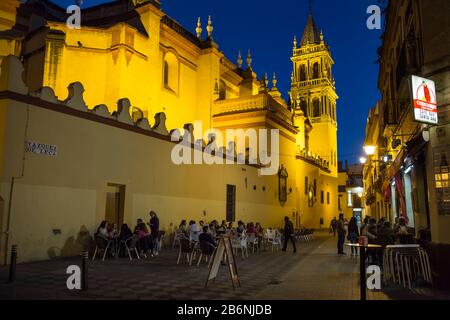 Night horizontal shot of Santa Ana church, surrounded by terraces of tapas' bars at Vazquez de Leca St in Triana district, Seville, Spain Stock Photo