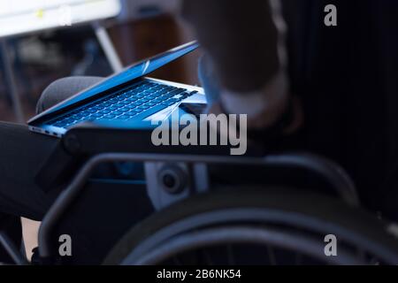 Disabled businessman in the wheelchair works in the office at the computer while performing in co-working space. Disability and handicap concept. Hori Stock Photo