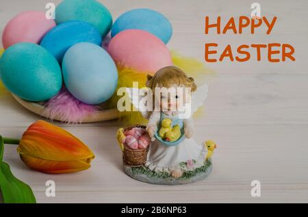 Easter card background. Easter angel with colorful eggs and chickens on a white wooden background with the inscription Happy Easter. Side view. Stock Photo