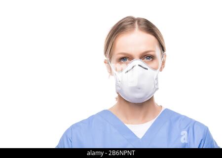 Portrait of attractive young nurse in respiratory mask and scrubs standing against white background Stock Photo