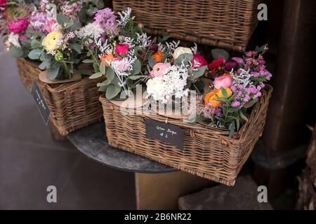 Bouquet of white ranunculus, red daisies, eucalyptus, blue hyacinths, white cherry in a wicker willow box for sale Stock Photo