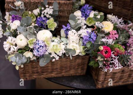 Bouquet of white ranunculus, red daisies, eucalyptus, blue hyacinths, white cherry in a wicker willow box for sale Stock Photo