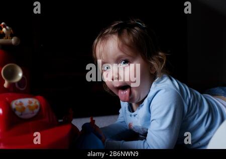 Cheeky 3 year old girl portrait having fun at home sticking her tongue out at the camera Stock Photo