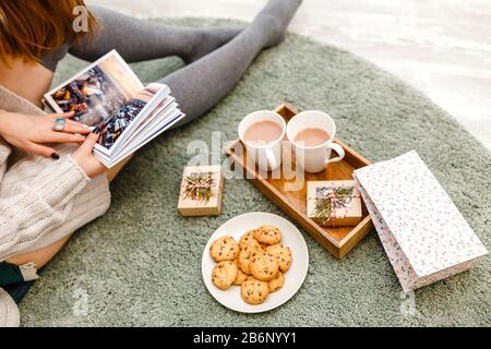 A woman considers an album with photos and drinks coffee with cookies, a concept of cozy leisure at home Stock Photo