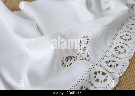 White natural cotton fabric with embroidery and lace with soft folds lies on an old wooden table Stock Photo