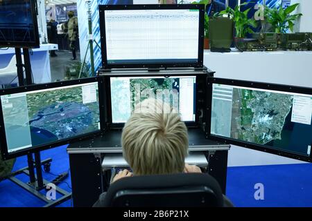 Young man sitting in front of monitors and working with military computer-assisted dispatch station for reconnaissance and coordination units. October Stock Photo
