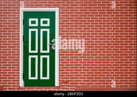Regular brick wall with white grouting surrounding a green door with white trim Stock Photo