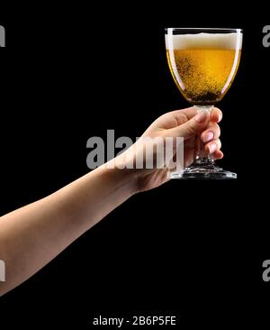 Woman hand holding lager beer glass isolated on black. Stock Photo