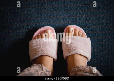 female legs with a pedicure in pink fluffy slippers on a dark blue carpet background. Copy space, flat lay, minimalism. Stock Photo