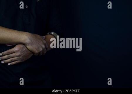 Young man praying with arms across posture. Islamic praying concept on black background. Selective focus on finger Stock Photo