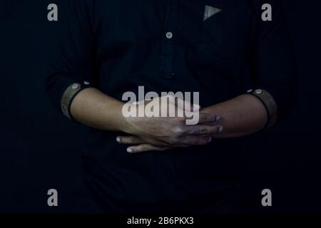 Young man praying with arms across posture. Islamic praying concept on black background. Selective focus on finger Stock Photo