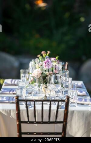 Table set for a wedding celebration with white tablecloth, crystal glasses and flowers in an outdoor setting in a garden Stock Photo