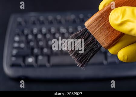 Cleaning the keyboard from dust and dirt with a brush. Maintenance and cleaning of computer hardware. Dark background. Stock Photo