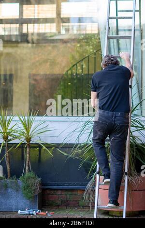 A Builder climbing a ladder to carry out repair work Stock Photo