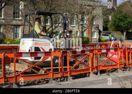 a builder or construction worker sitting on a digger during construction work digging up the road Stock Photo