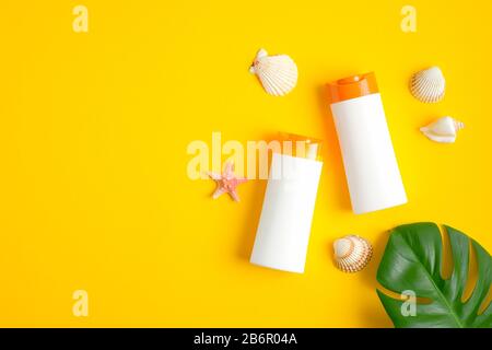 Two white plastic sunscreen lotion bottles, seashells and tropical leaf on yellow background. Sun protection, sunscreen cosmetic product, summer skin Stock Photo