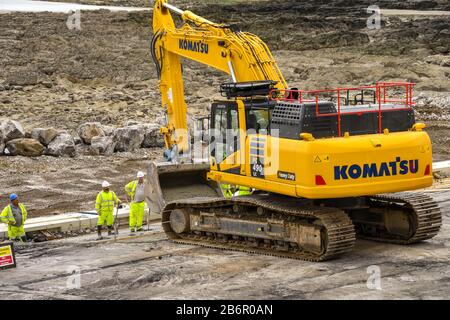 PORTHCAWL, WALES - JUNE 2018: Heavy duty excavator carrying ready mixed concrete in its bucket to workers who are strengthening the seafront Stock Photo