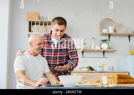 Young man and senior father using phone in the kitchen Stock Photo