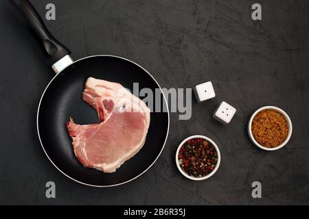 Raw pork loin chops in rustic skillet on black background Stock Photo