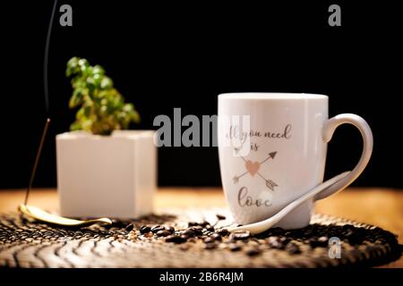 White ceramic cup with the words "all you need is love" full of black coffee on a wooden table, and coffee grains Stock Photo
