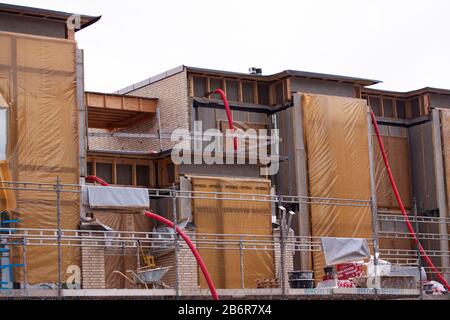 New low-rise residential building under construction wth red pipes sticking out and covered window sections: Copenhagen, February 27 - 2020. Stock Photo