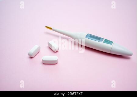 Digital thermometer and white pills isolated on pink background. Epidemic, painkillers, healthcare and treatment concept. With copy space. Stock Photo